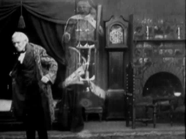 Scrooge, in his dressing gown, stands beside the double-exposed Ghost of Christmas Present in A Christmas Carol (1910)