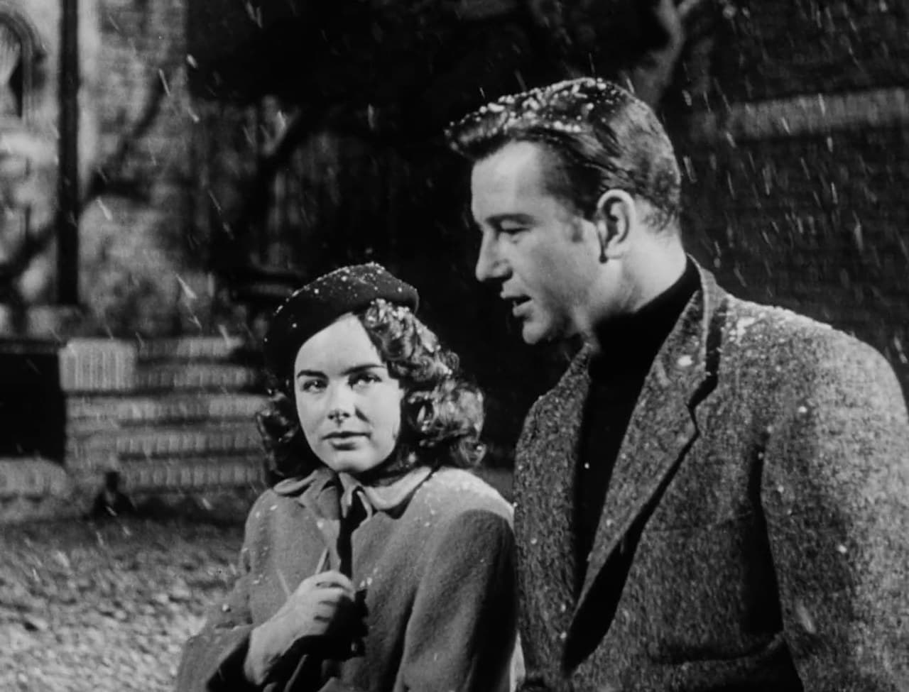 Terry Moore and Tom Drake talk as snow falls outside a brick house in The Great Rupert (1950)