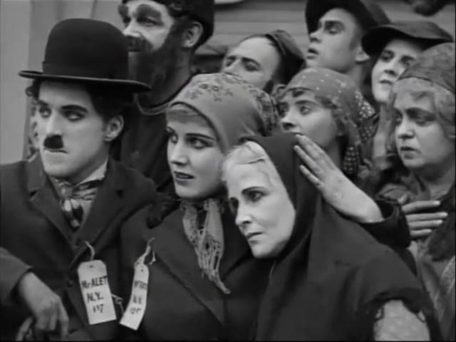 Charlie Chaplin, wearing an immigration tag, stands among newly arrived passengers beside Edna Purviance in The Immigrant (1917)